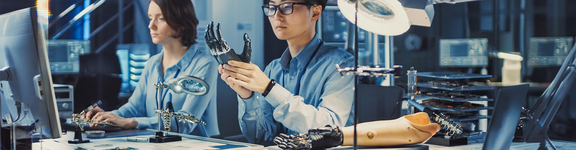 Scientist sitting at desk analyzing robot hand